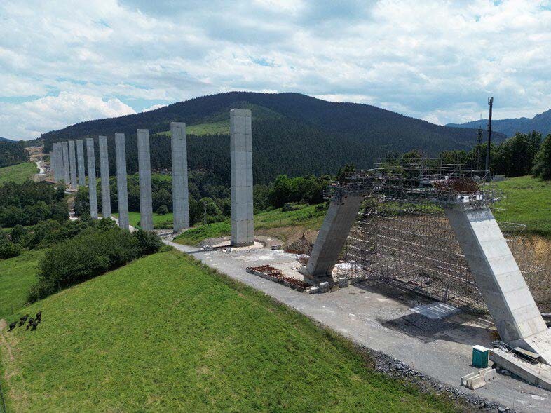 Obras de la Y Vasca - Pilares de viaducto en construcción Obras de la Y Vasca - Pilares de hormigón alineados sobre un valle verde durante la fase inicial de construcción de un viaducto, con andamios...